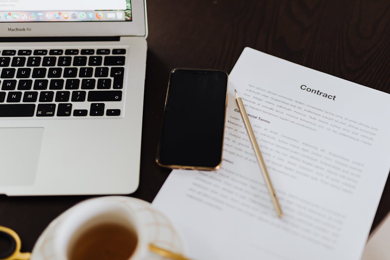 Close-up of a workspace with a contract, laptop, smartphone, and cup of tea.